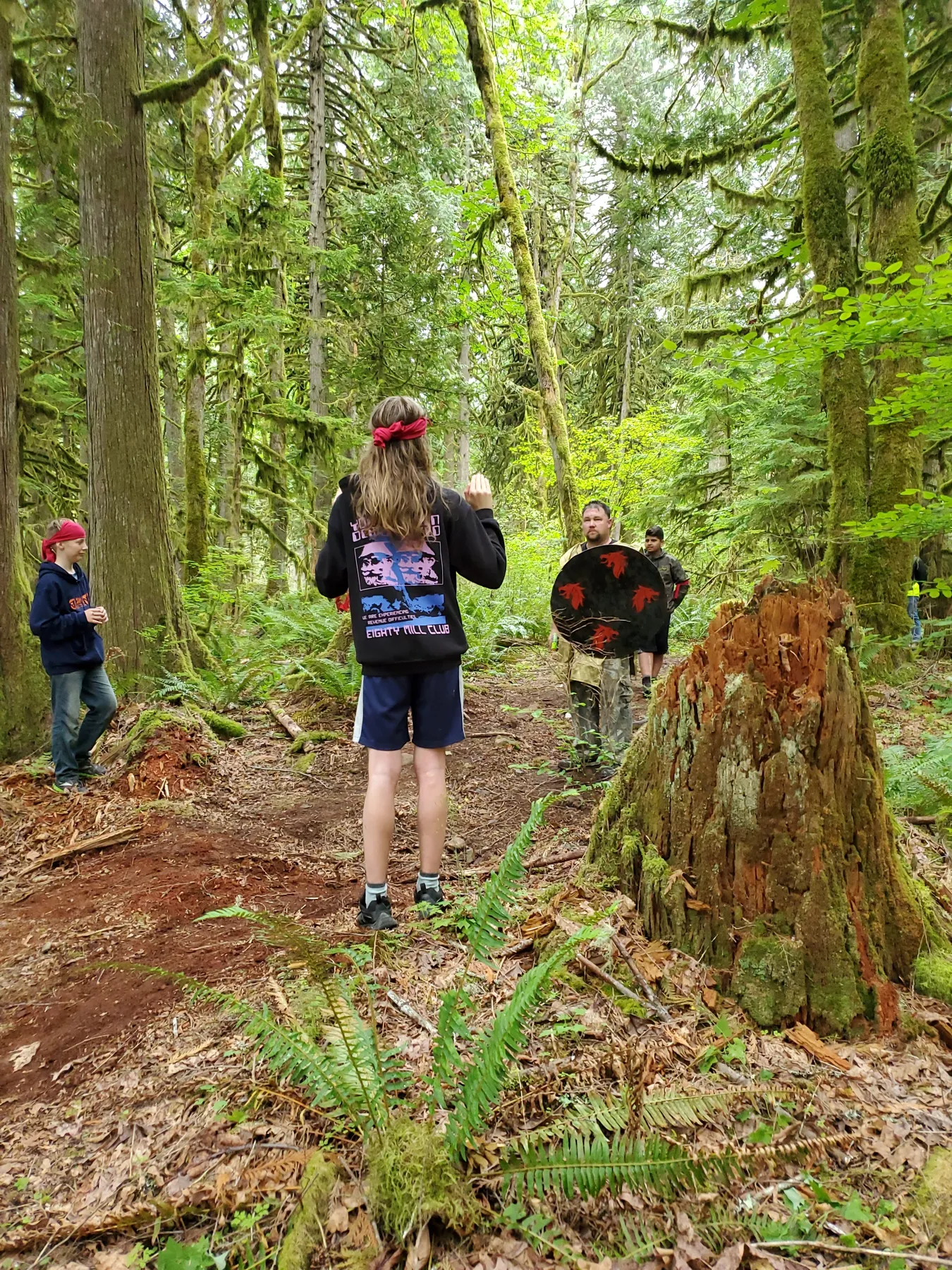 A young man stands on a mossy stump, facing the forest