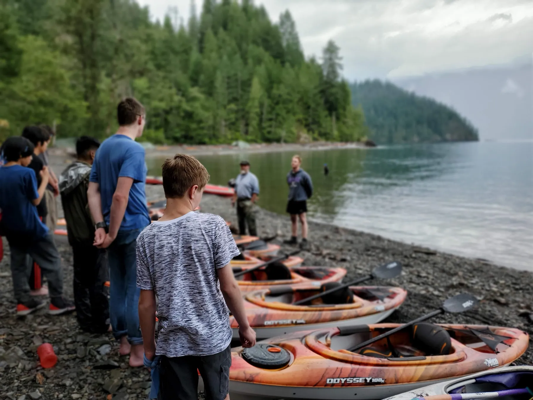 Orange kayaks lined up on the shore, young men at the water